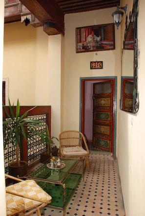 Un intérieur chaleureux, décoré dans un style marocain traditionnel, avec une porte ornée de motifs, un fauteuil en osier et une table verte sur laquelle est posé un plateau.