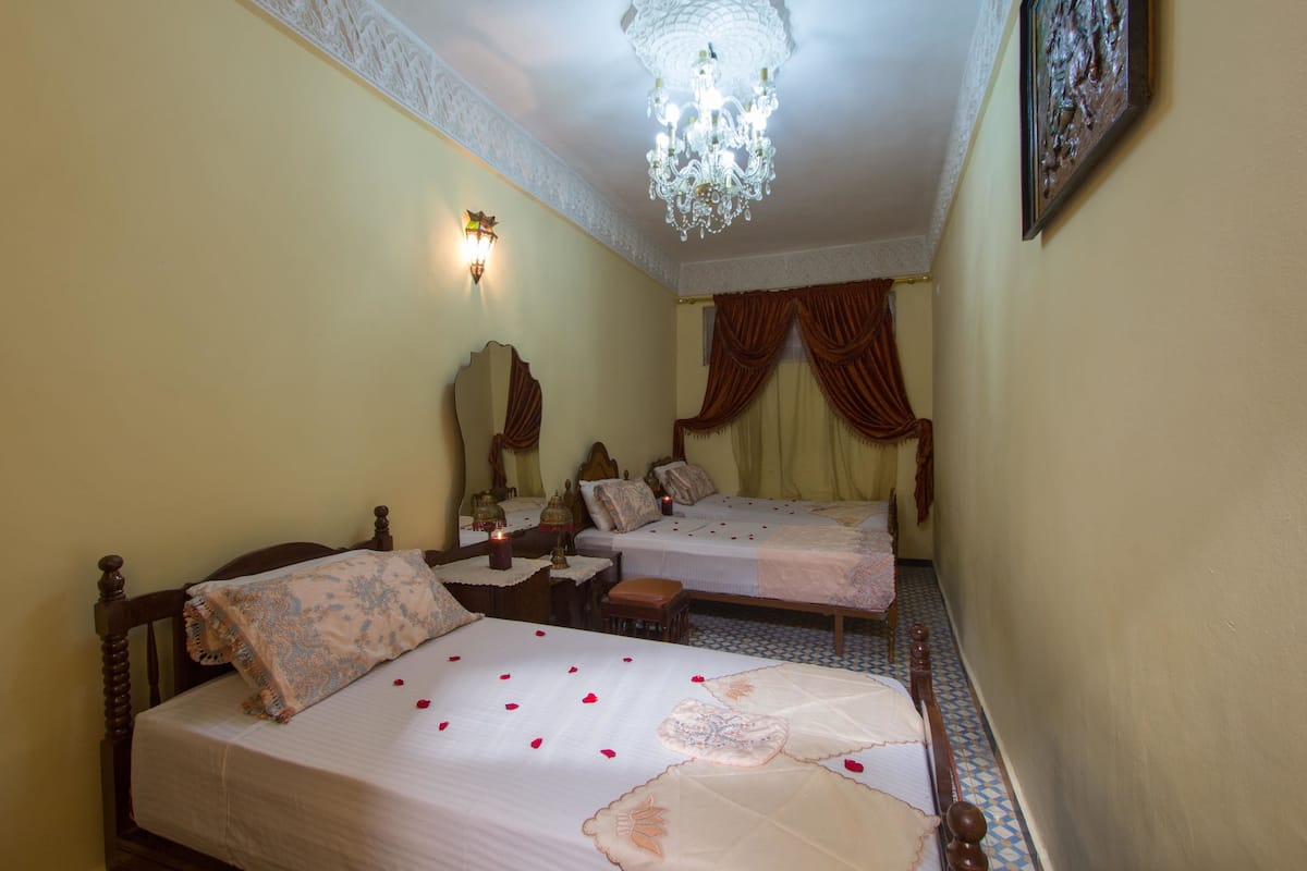 A hotel room with two beds, a chandelier, a mirror, and a picture on the wall.