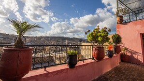 Una terraza en la azotea con plantas en macetas, barandilla de metal y vistas de la ciudad.