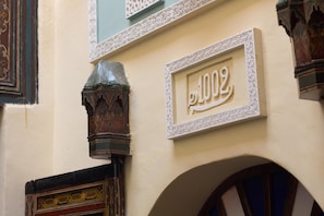 Une façade d’immeuble ornée d’un numéro « 1002 » décoratif, encadré de motifs blancs complexes.