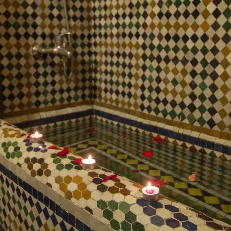 A bathroom with a mosaic tile wall and floor, a bathtub with candles, and a shower area.