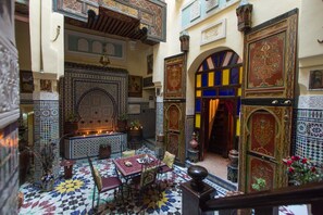 A Moroccan interior with a tiled floor, a central seating area, and ornate walls. - Riad La Source Bleue (Fes)