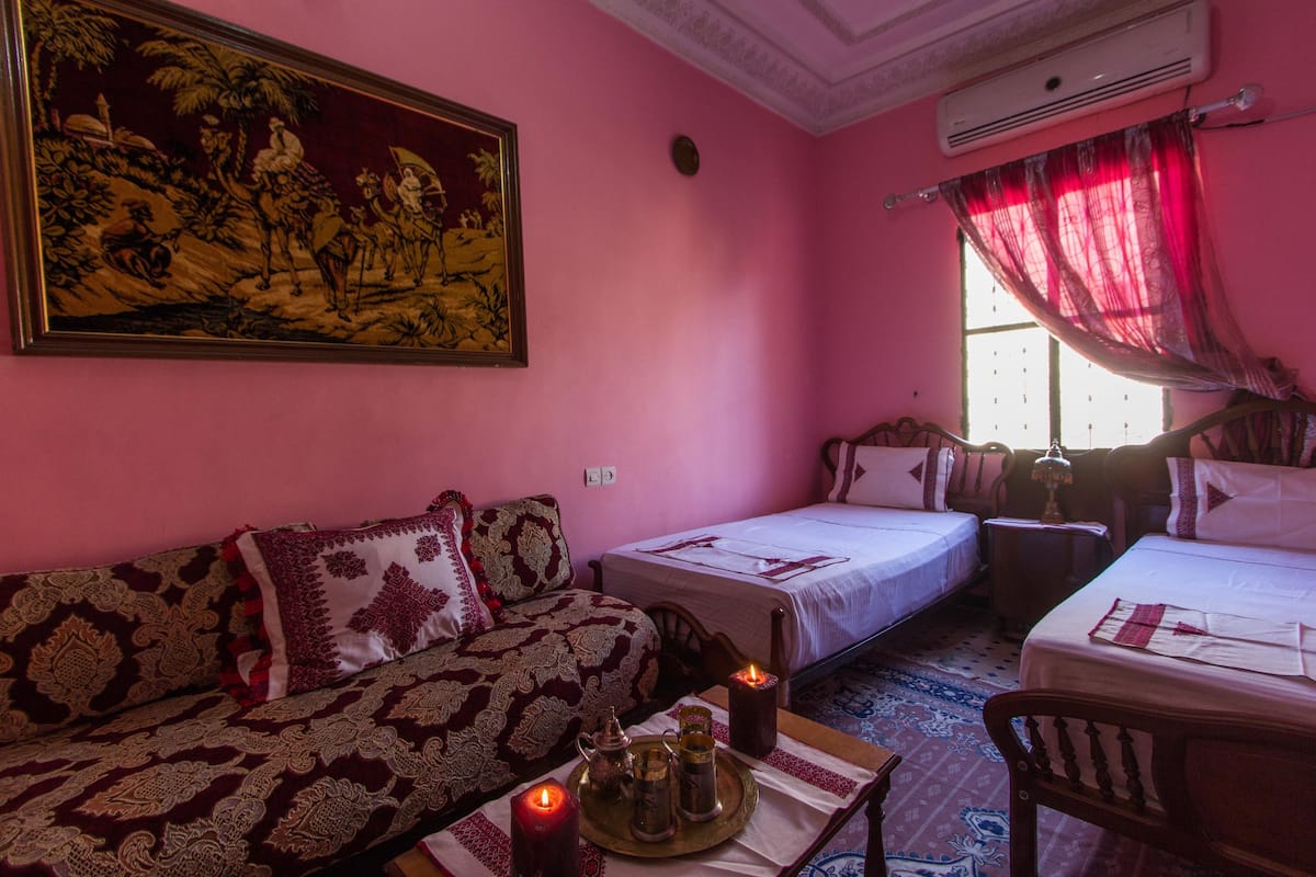 A room with two beds, a sofa, a table with a candle, and a large painting on the wall.