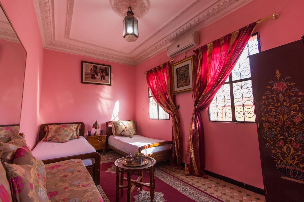 A pink-themed room with two beds, a sofa, a small table, and decorative elements.