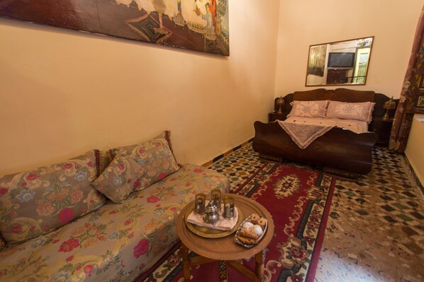 A living room with a sofa, a coffee table with snacks, a patterned rug, and a painting on the wall. - Riad La Source Bleue (Fes)