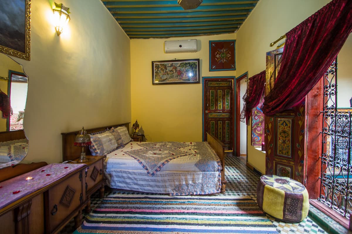 A bedroom with a bed, a dresser, a mirror, and a window with curtains.