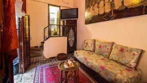 Una sala de estar con un sofá, un televisor, un tapete estampado y una escalera.