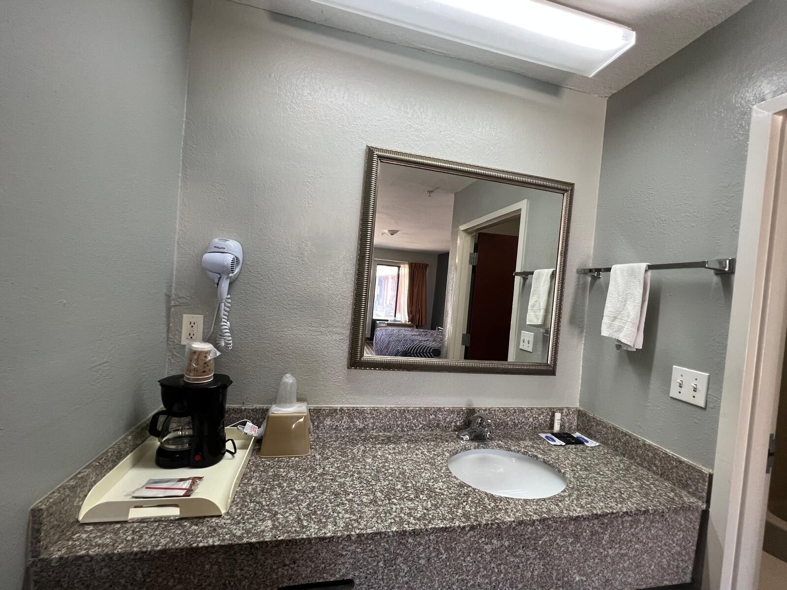 Une salle de bain d’hôtel avec un comptoir en granit, un lavabo, un sèche-cheveux, un miroir et un porte-serviettes.