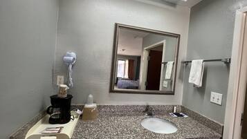 Une salle de bain d’hôtel avec un comptoir en granit, un lavabo, un sèche-cheveux, un miroir et un porte-serviettes.