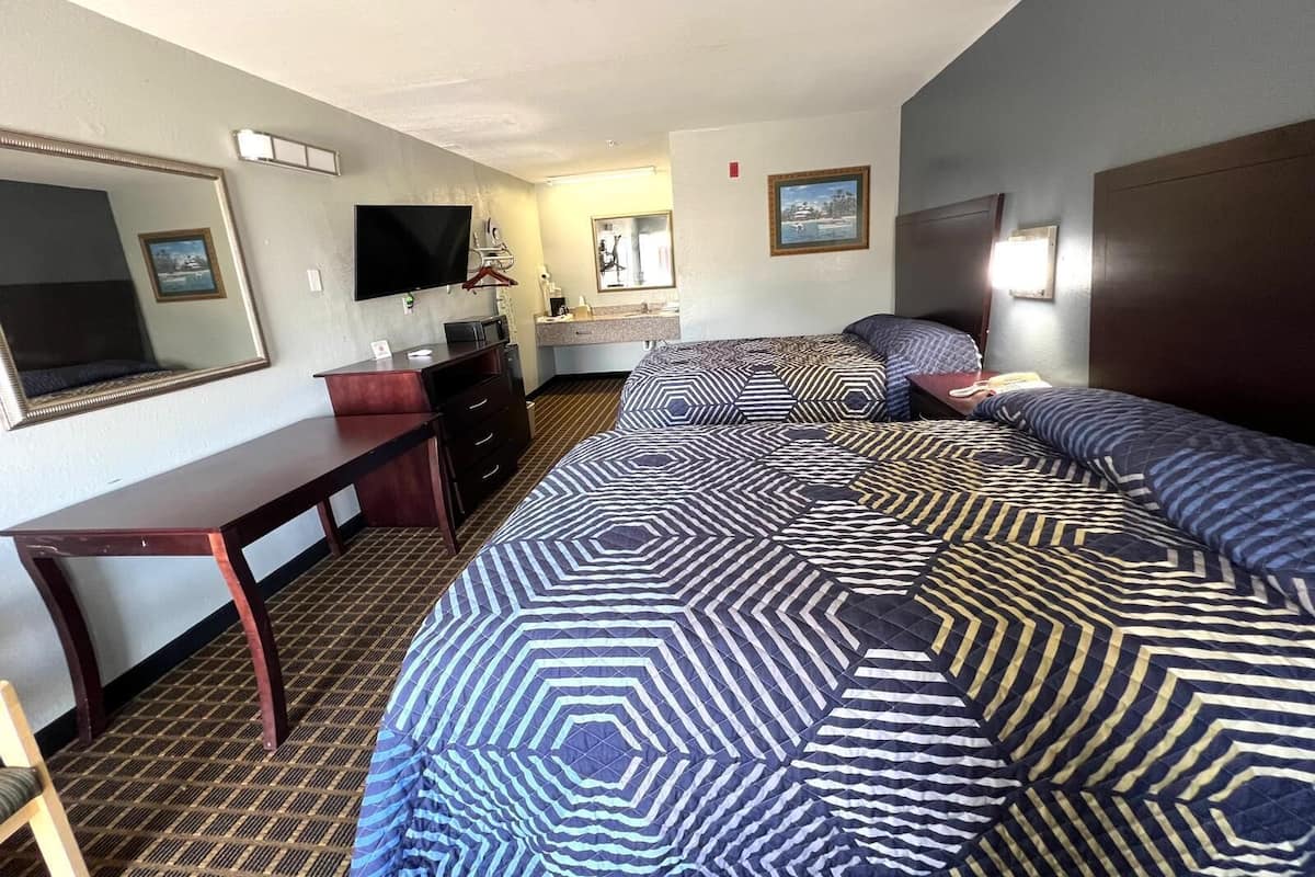 Quarto de hotel com uma cama grande, uma escrivaninha, uma televisão e um banheiro visível ao fundo.