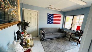 A living room with a grey sofa, a coffee table with decorative items, a white door, and an American flag on the wall.