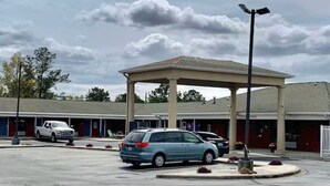 A parking lot with a covered pavilion, a row of hotel rooms, and a few parked cars.