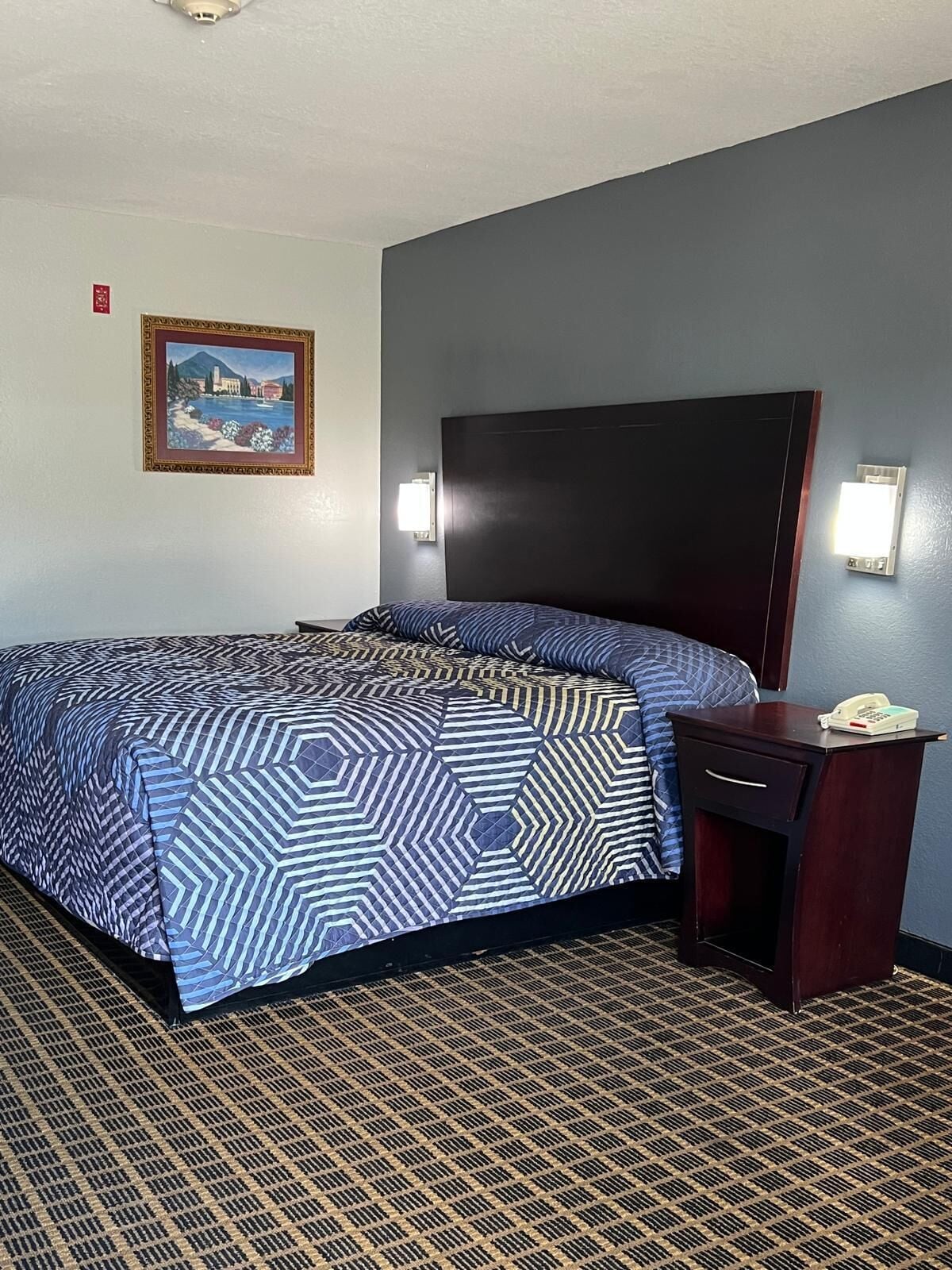 Une chambre d’hôtel avec un lit, une table de chevet, un téléphone et un tableau au mur.