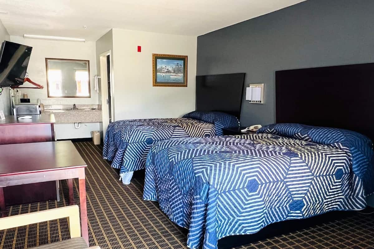 Quarto de hotel com duas camas, uma escrivaninha, um espelho, uma televisão e um quadro na parede.