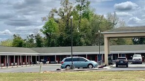 A motel with a covered parking area, multiple rooms, and a lawn in front.