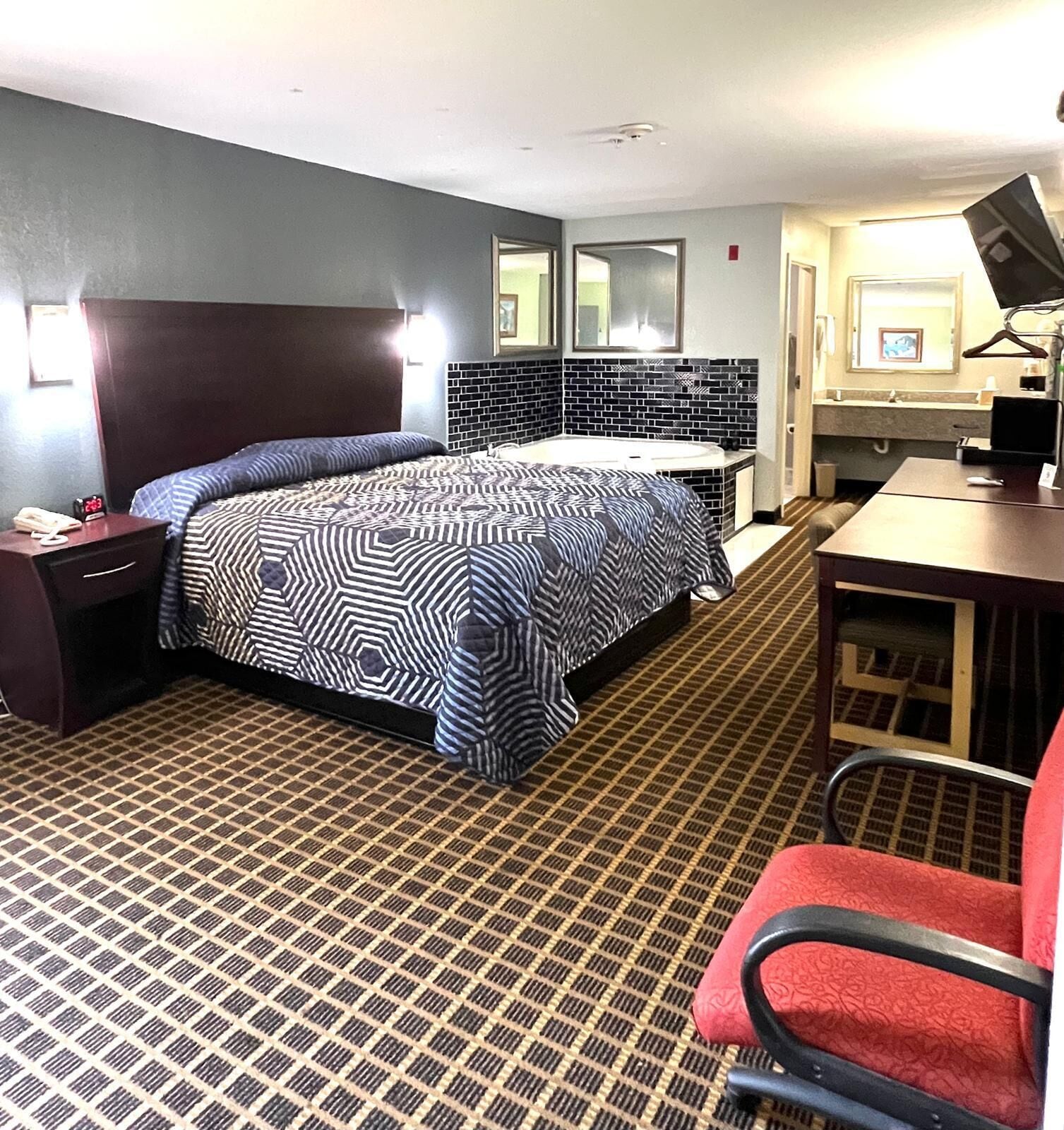 Habitación de hotel con cama, escritorio, silla, baño y espejo.