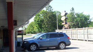 A blue SUV parked under a covered area with a wooden fence and trees in the background. - Lakeridge Motel (Whitby)