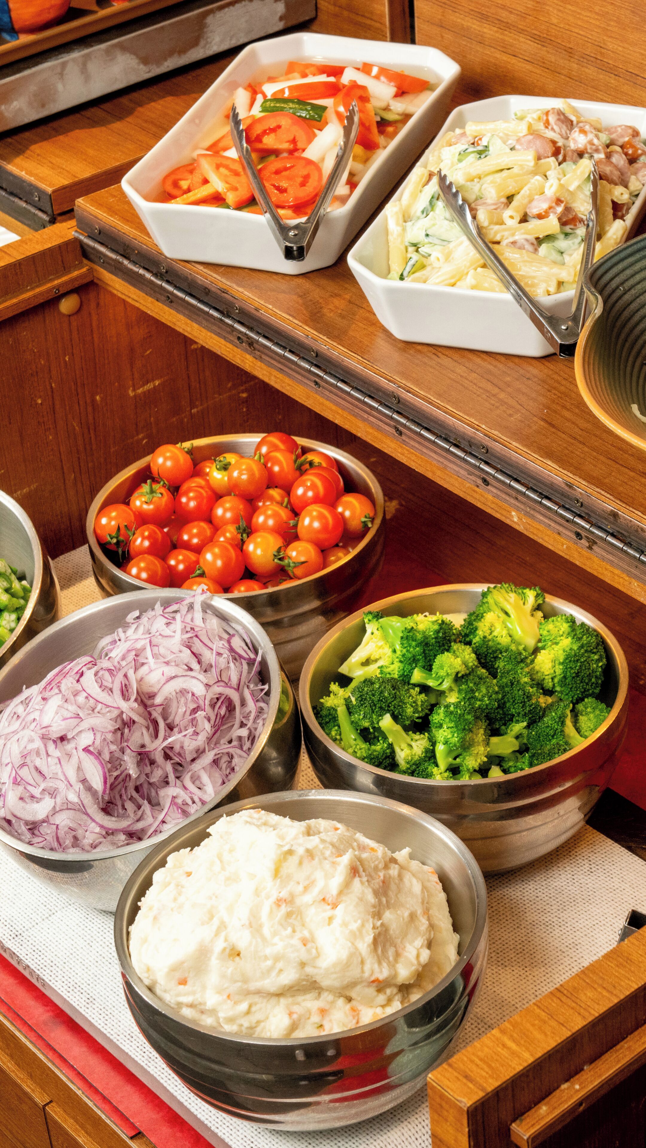 A buffet table with various food items including tomatoes, onions, broccoli, and a creamy dish.