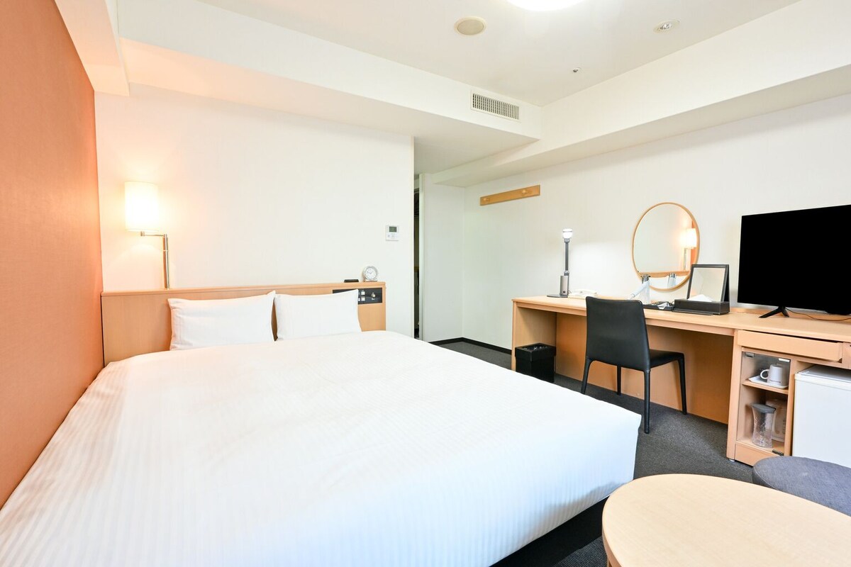 Une chambre d’hôtel avec un grand lit, un bureau avec un ordinateur, une chaise, une télévision et une petite table.