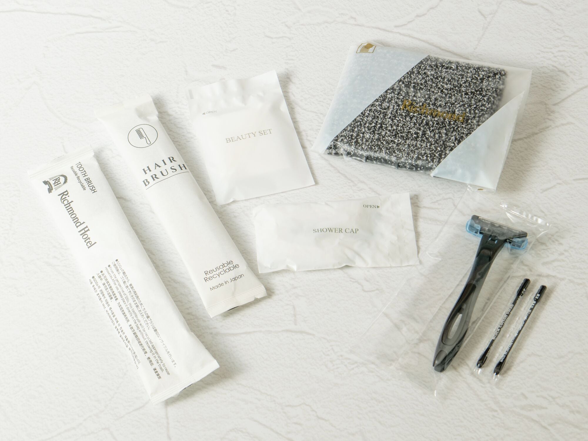 Artigos de higiene pessoal, incluindo escova de dentes, escova de cabelo e touca de chuveiro, tudo embalado em branco.