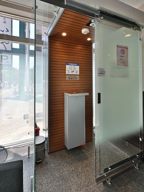 A modern office space with a glass partition, a wooden panel wall, a fire extinguisher, and a sign indicating a smoking area. - Richmond Hotel Hakataekimae (Fukuoka)