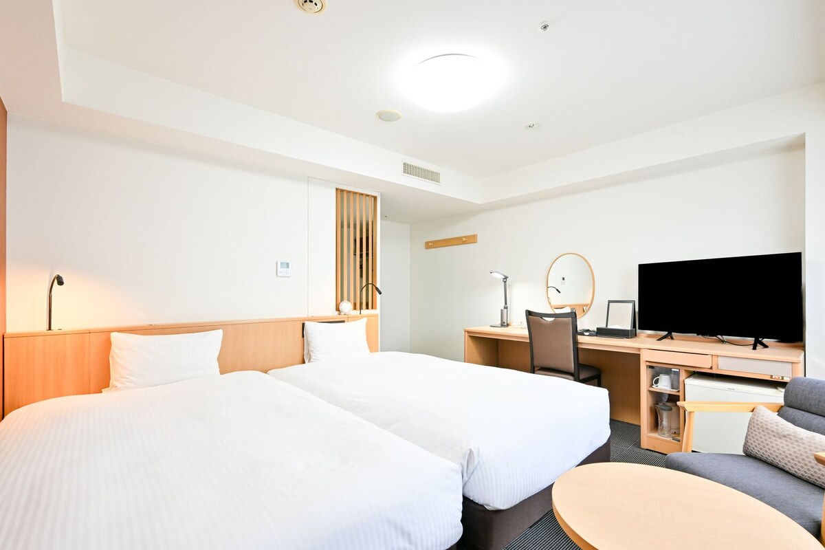 Une chambre d’hôtel avec deux lits, un bureau avec un ordinateur, une télévision et une petite table ronde.