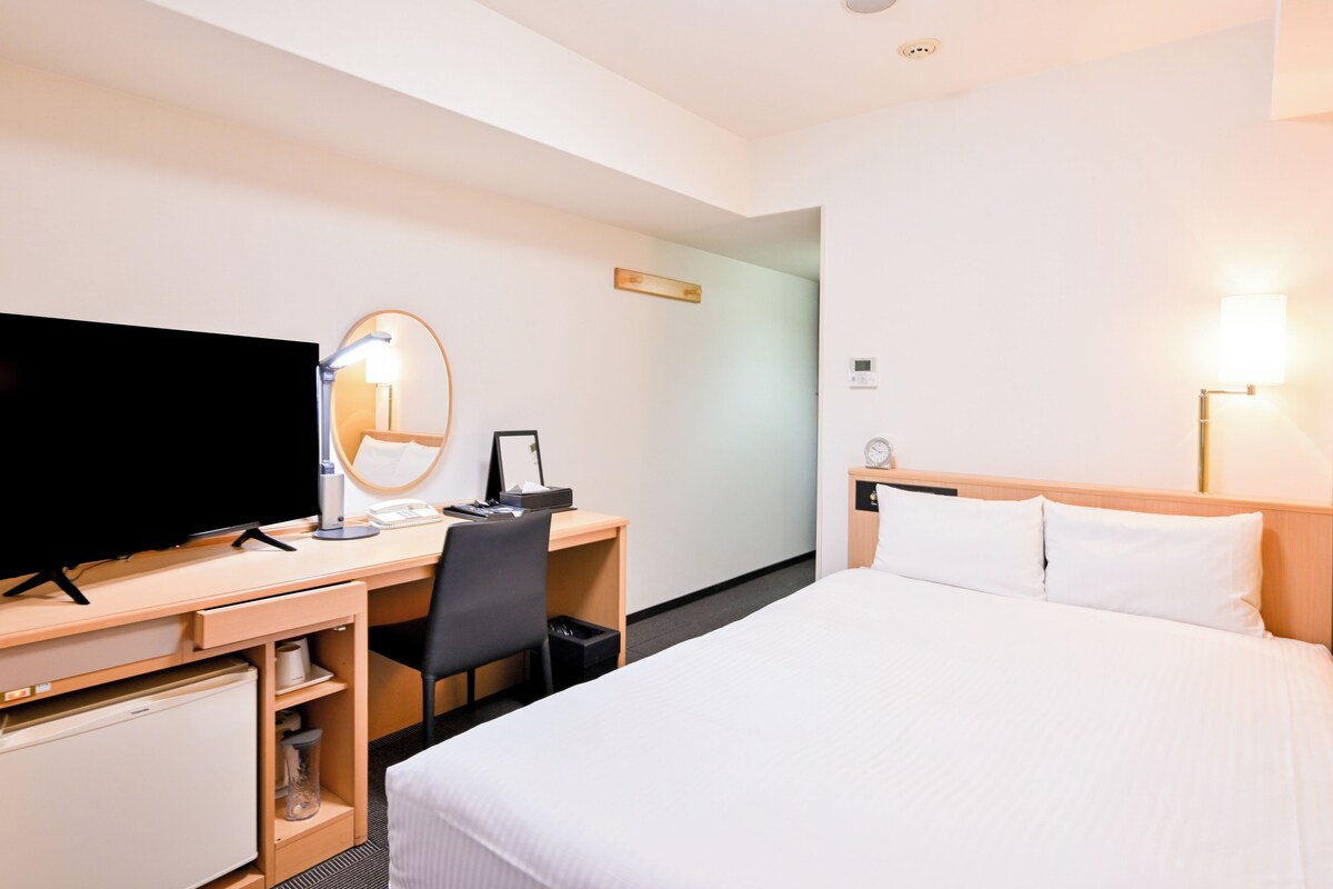 Une chambre d’hôtel équipée d’un lit, d’un bureau, d’une chaise, d’une télévision et d’un miroir.
