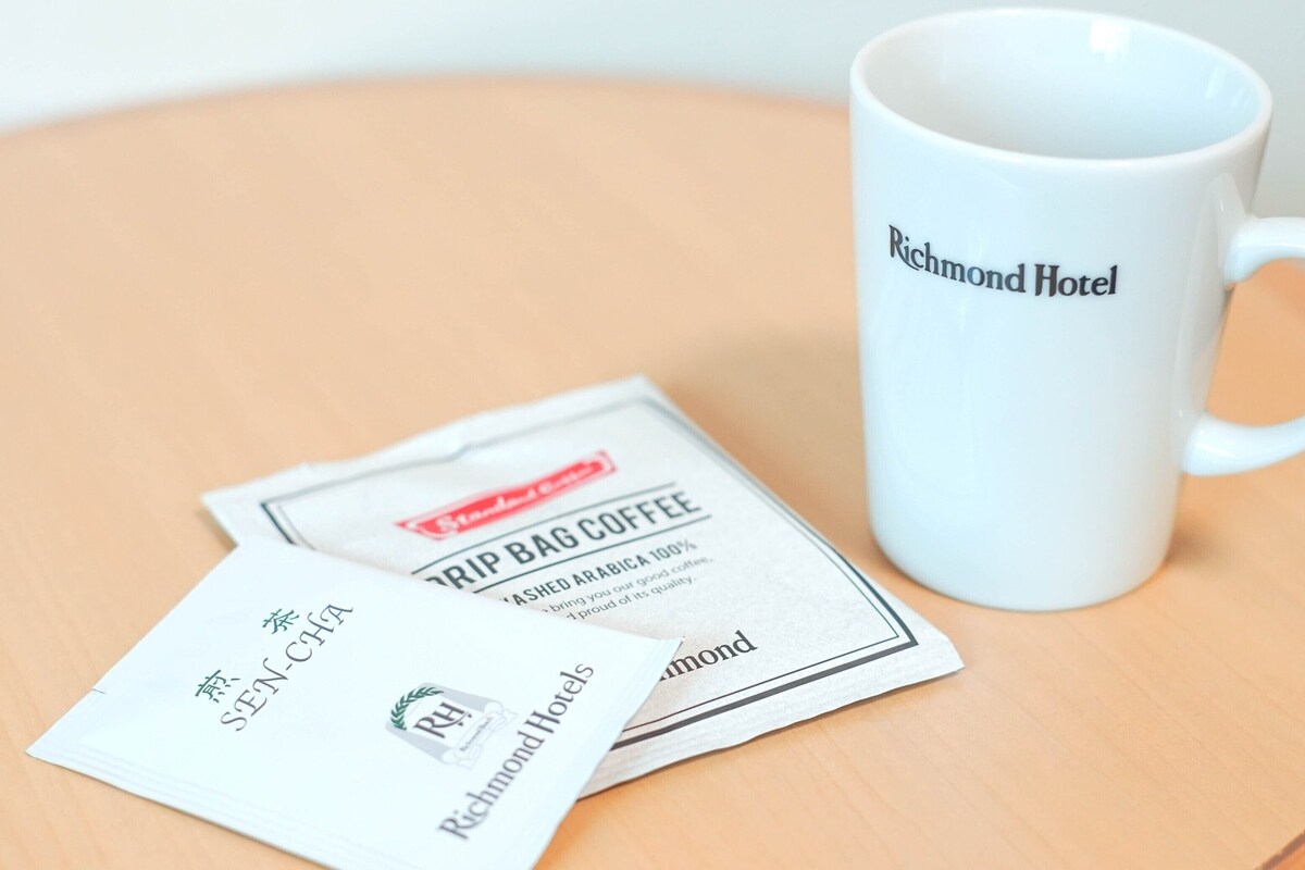 Une tasse blanche portant l’inscription « Richmond Hotel » et deux sachets de café, le tout posé sur une surface en bois.