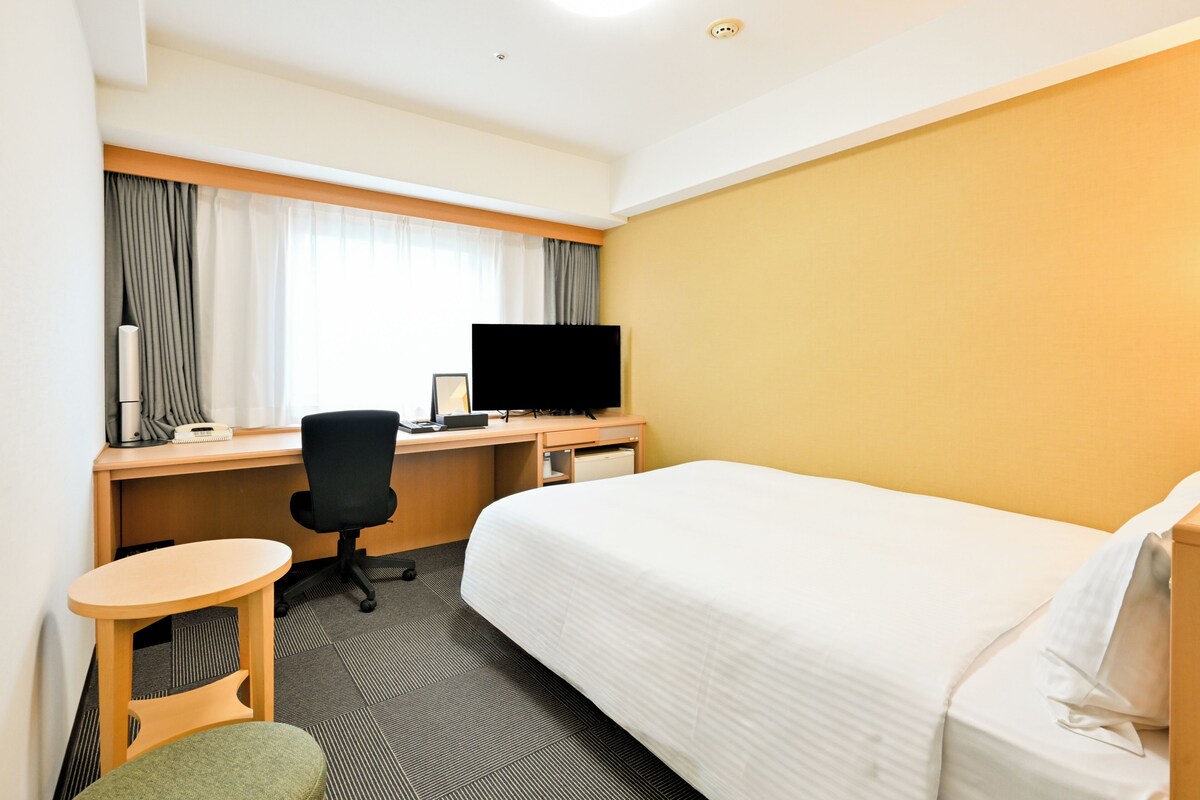 Une chambre d’hôtel équipée d’un lit, d’un bureau, d’une chaise, d’une télévision et d’une petite table.