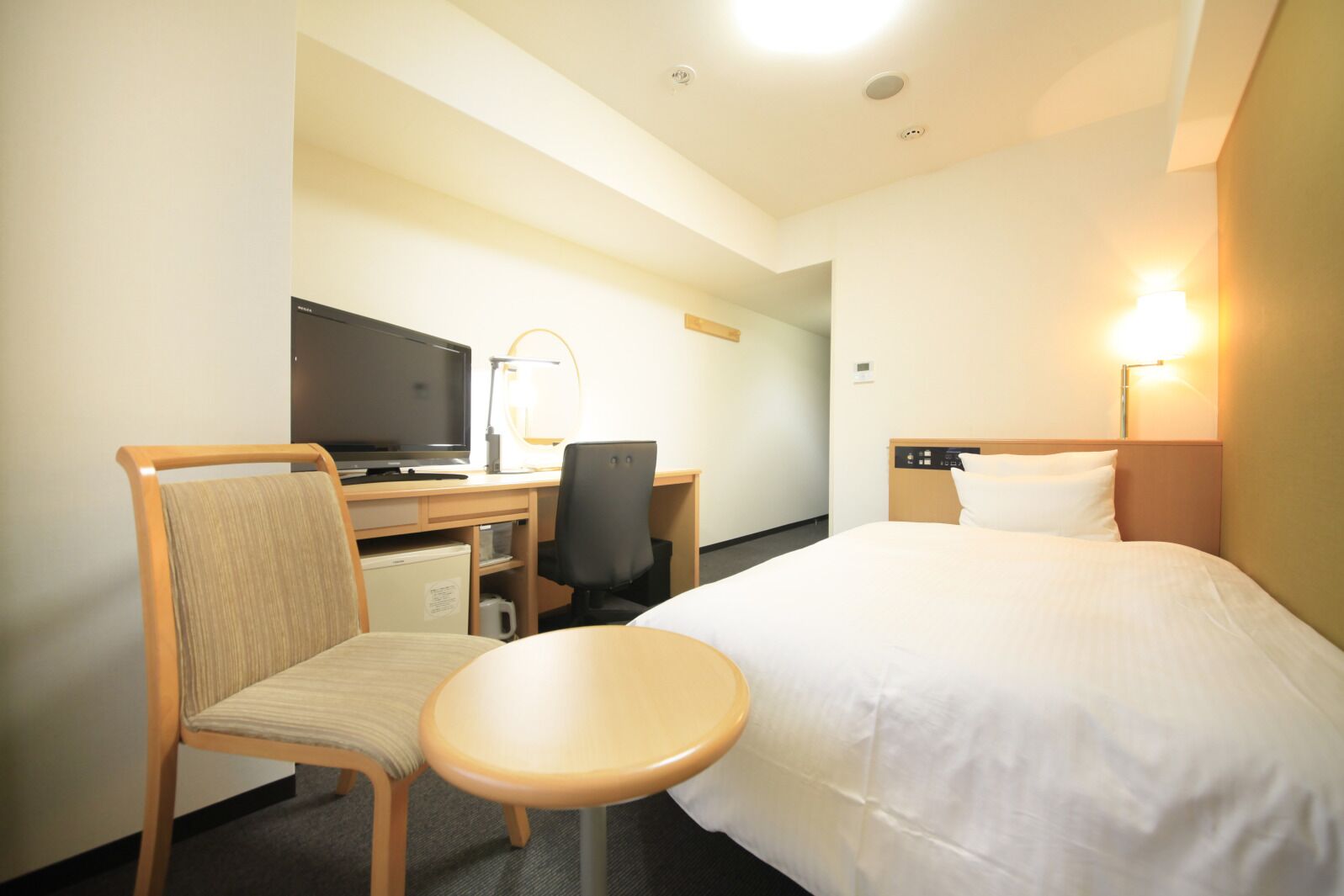 A hotel room with a bed, desk, chair, television, and a small table.