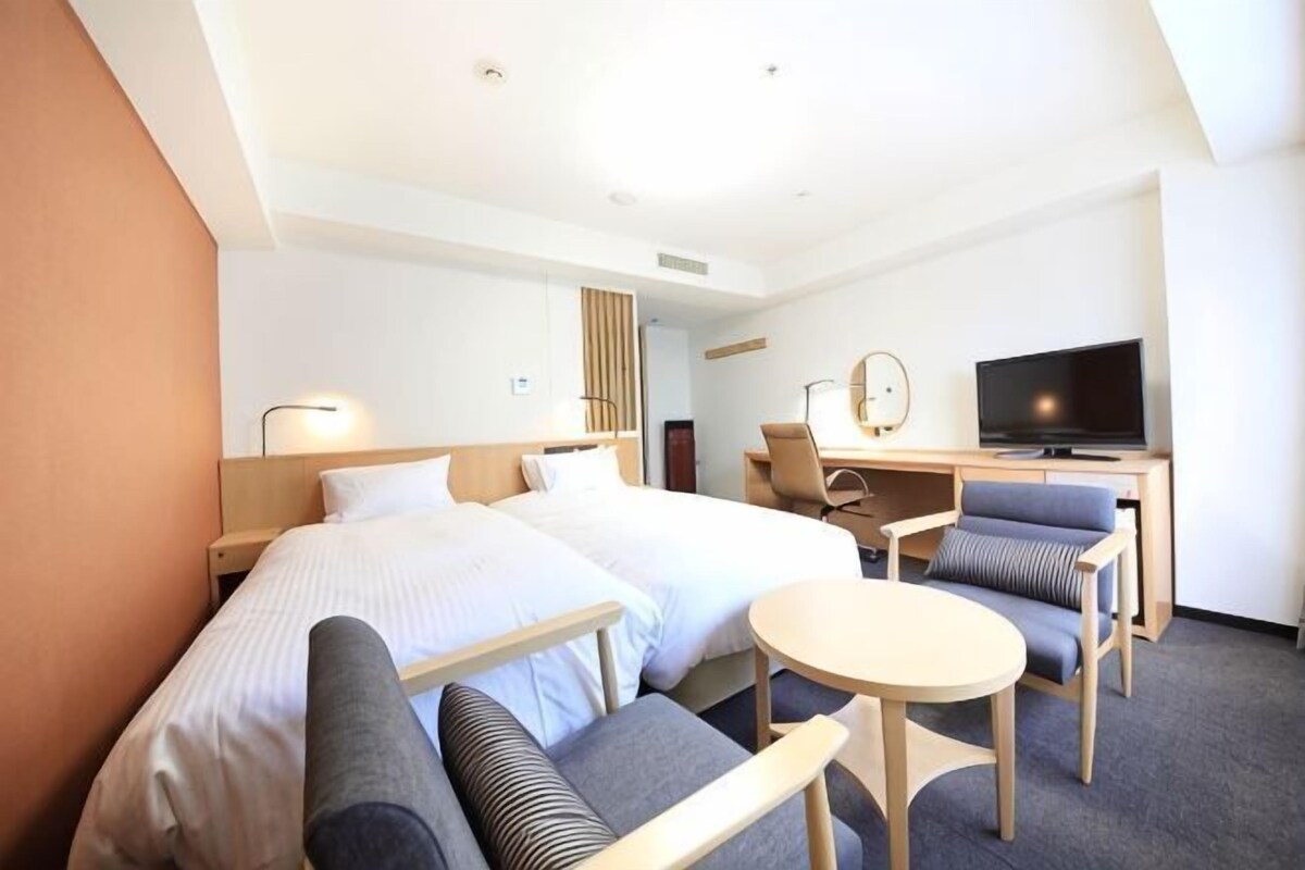 Une chambre d’hôtel avec deux lits, un bureau avec une télévision, une petite table ronde et un canapé.