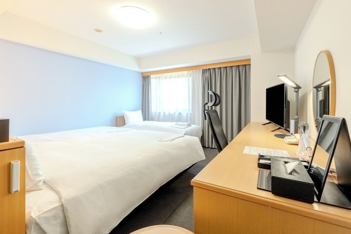 Une chambre d’hôtel équipée d’un lit, d’un bureau, d’une chaise, d’une lampe et d’un grand miroir.