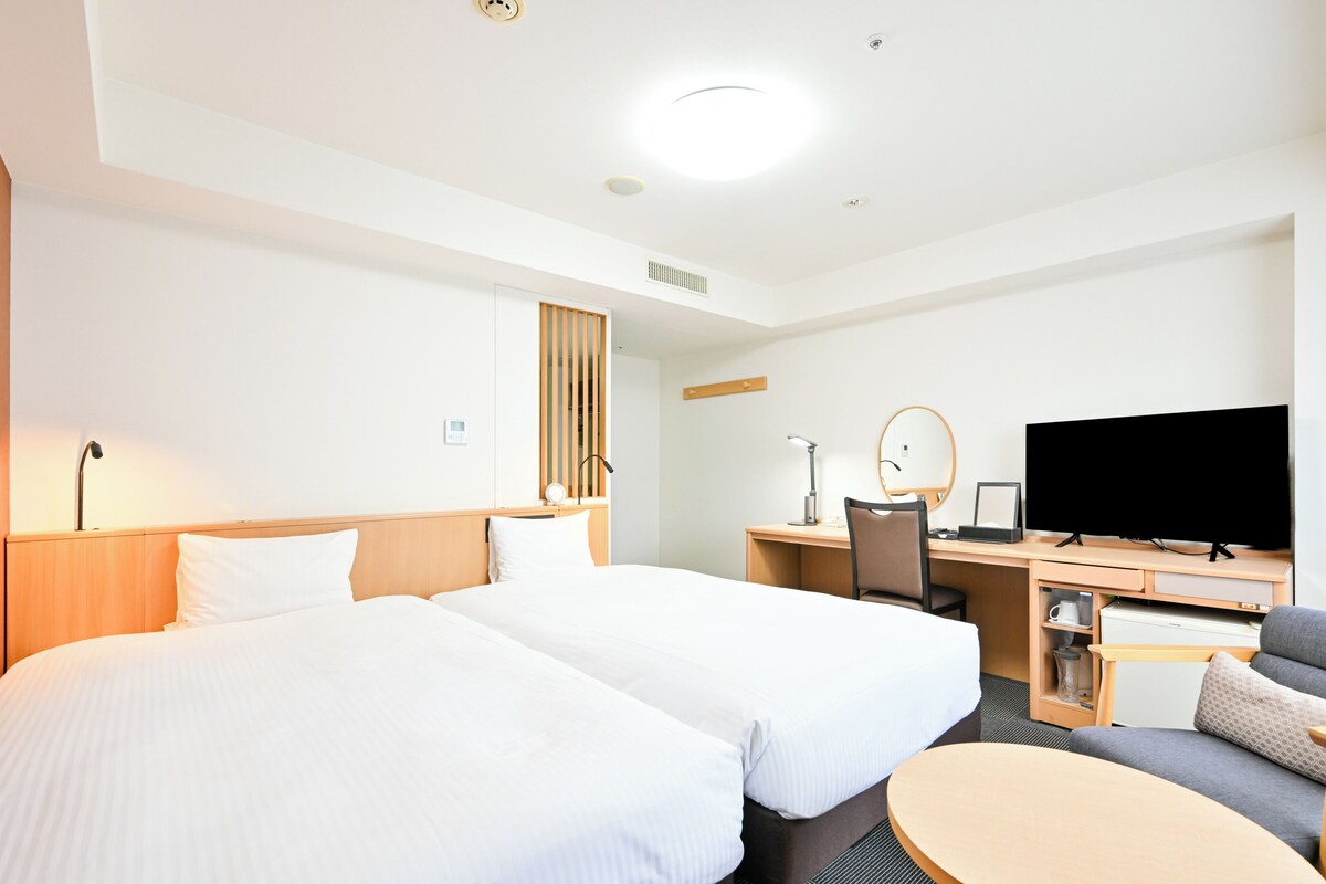 Une chambre d’hôtel avec deux lits, un bureau avec un ordinateur, une télévision et une petite table ronde.