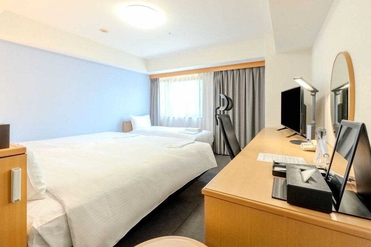 Une chambre d’hôtel équipée d’un lit, d’un bureau, d’une chaise, d’une télévision et d’un grand miroir.