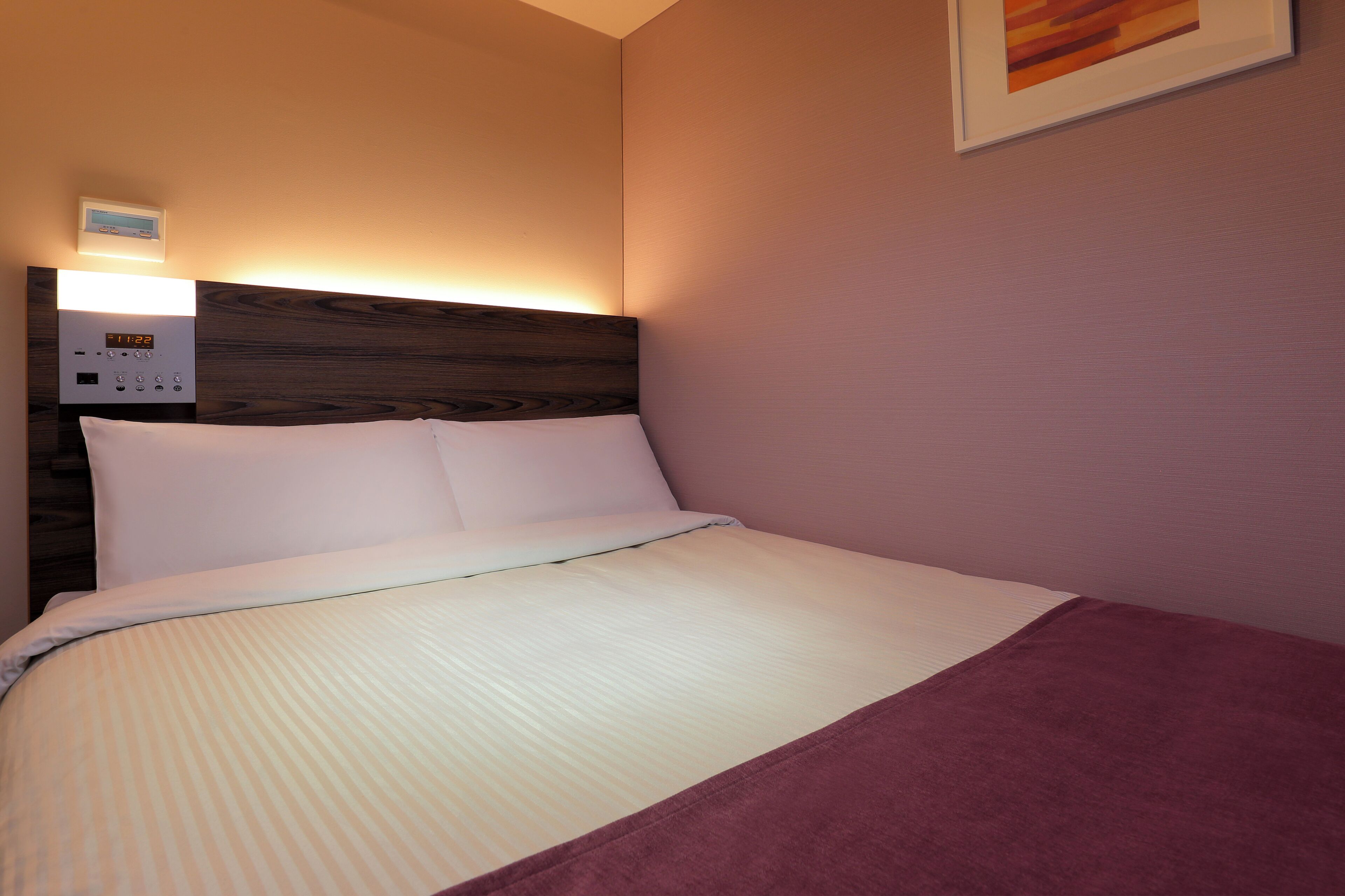 Una cama bien hecha con cabecera, un panel de control y un cuadro en la pared.