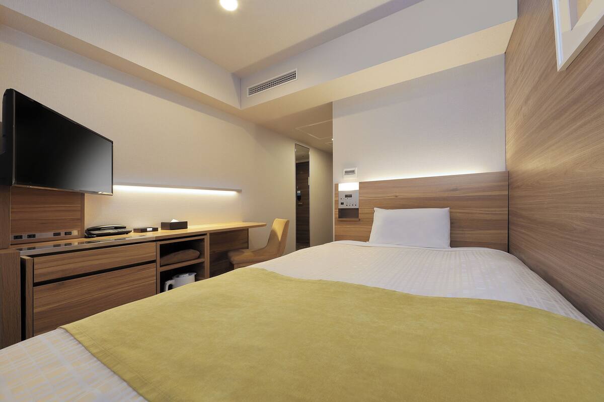 A hotel room with a bed, a desk, a chair, a television, and a bedside table.