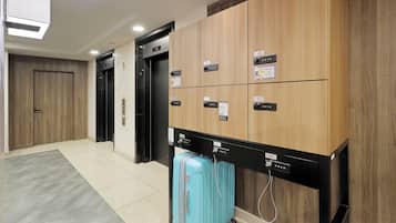 A hotel lobby with a wooden reception desk, numbered lockers, and a blue suitcase on wheels.