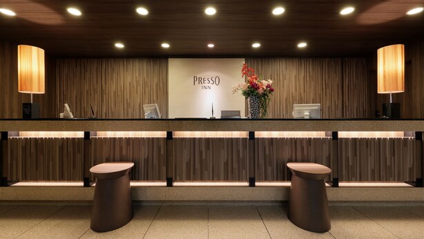 A reception area with a wooden panel wall, a reception desk, two round tables, and a floral arrangement. - Keio Presso Inn Ikebukuro (Tokyo)