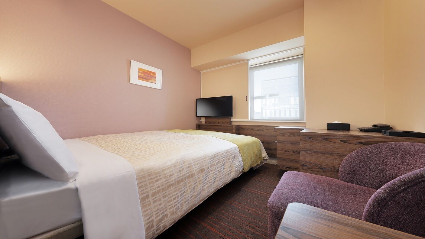 A hotel room with a bed, a desk, a chair, a television, and a window.