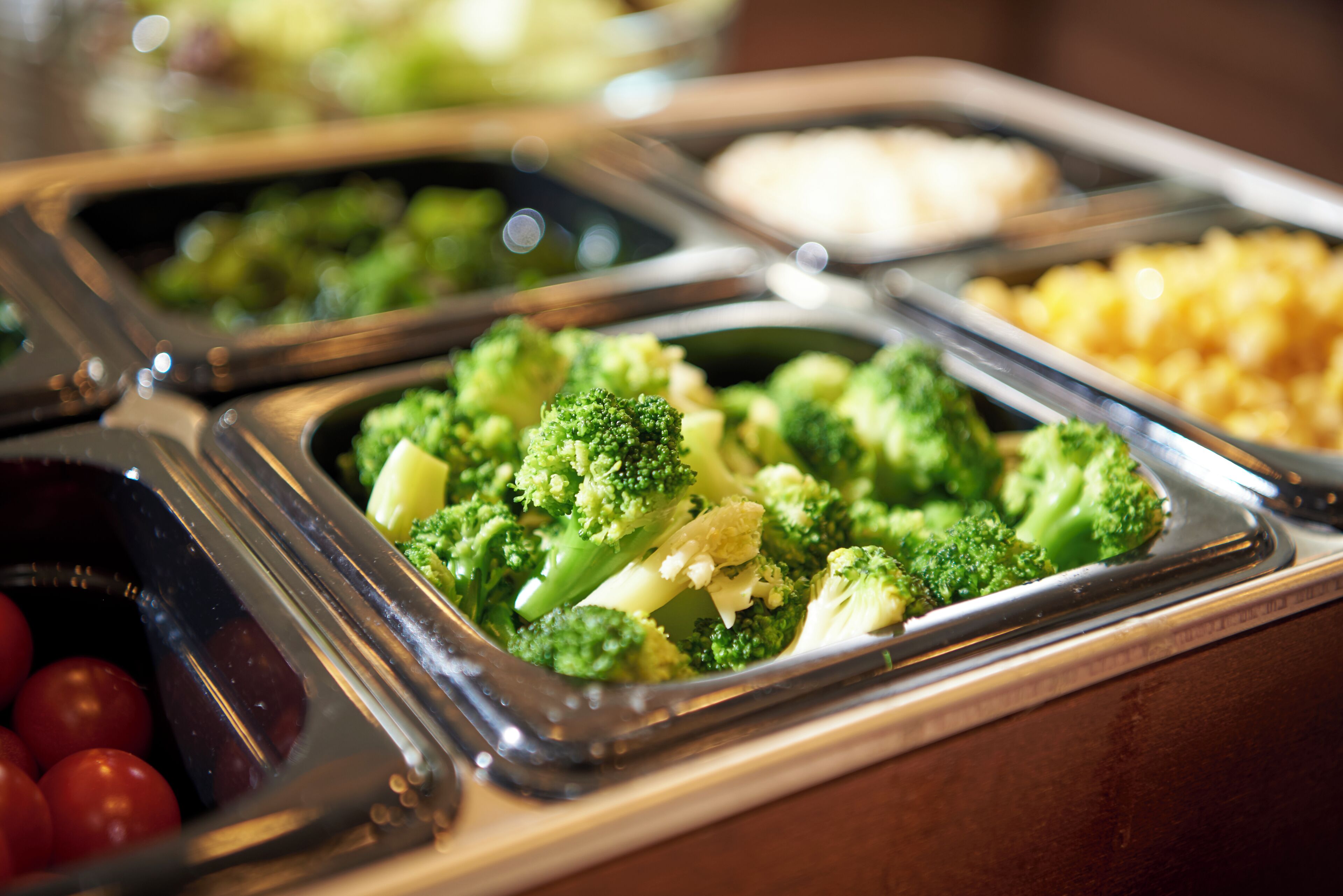 A buffet with various food options including broccoli, tomatoes, and macaroni.