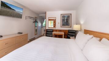 A hotel room with a large bed, a desk, a chair, a TV, and a painting on the wall.