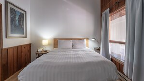 A neatly made bed with white linens, a wooden headboard, a bedside lamp, a telephone, and a framed picture on the wall. - Cedar Motel (Radium Hot Springs)