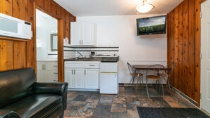 A compact kitchen with white cabinets, a refrigerator, a microwave, and a dining area with a table and chairs. - Cedar Motel (Radium Hot Springs)