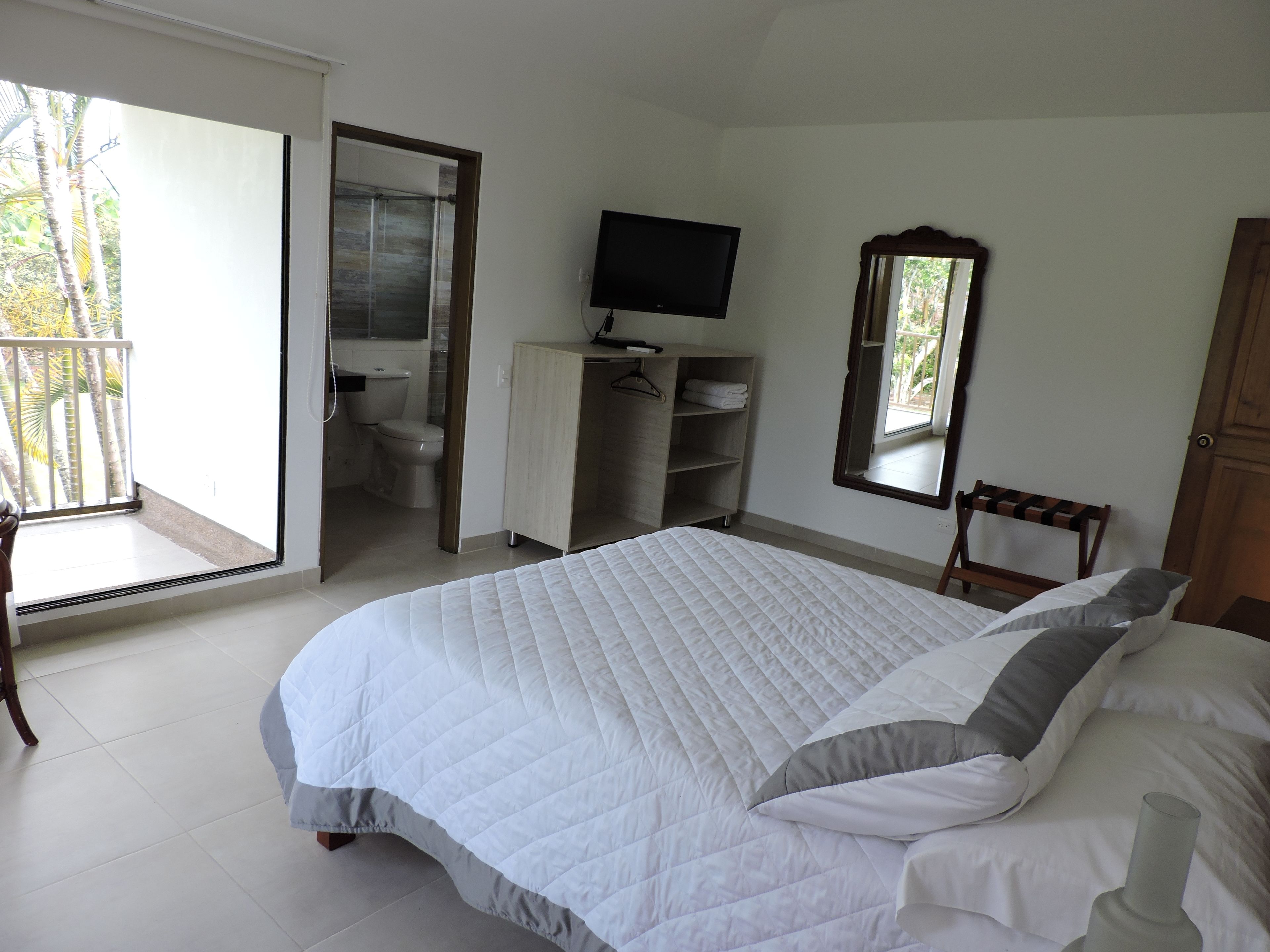 Une chambre à coucher avec un grand lit, une télévision, une armoire et une salle de bain visible à travers une porte ouverte.