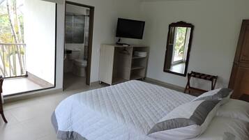 Une chambre à coucher avec un grand lit, une télévision, une armoire et une salle de bain visible à travers une porte ouverte.