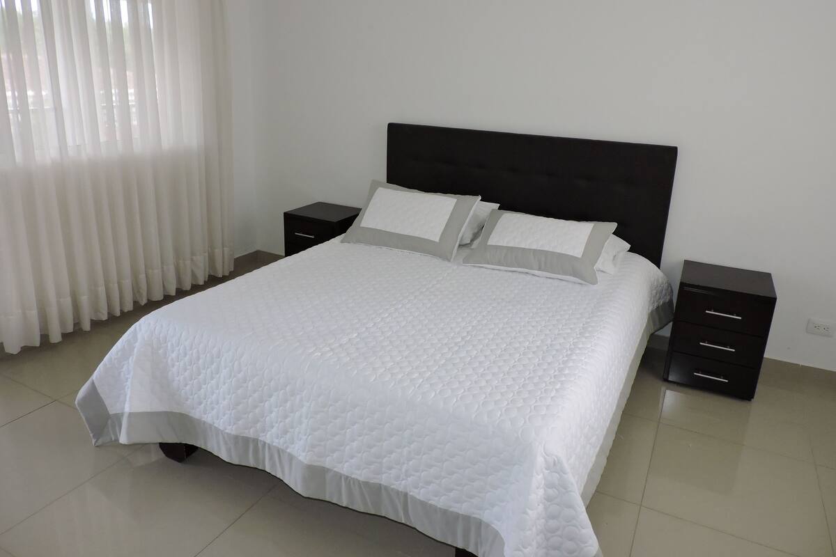 A neatly made bed with white bedding, a black headboard, and two bedside tables with drawers.