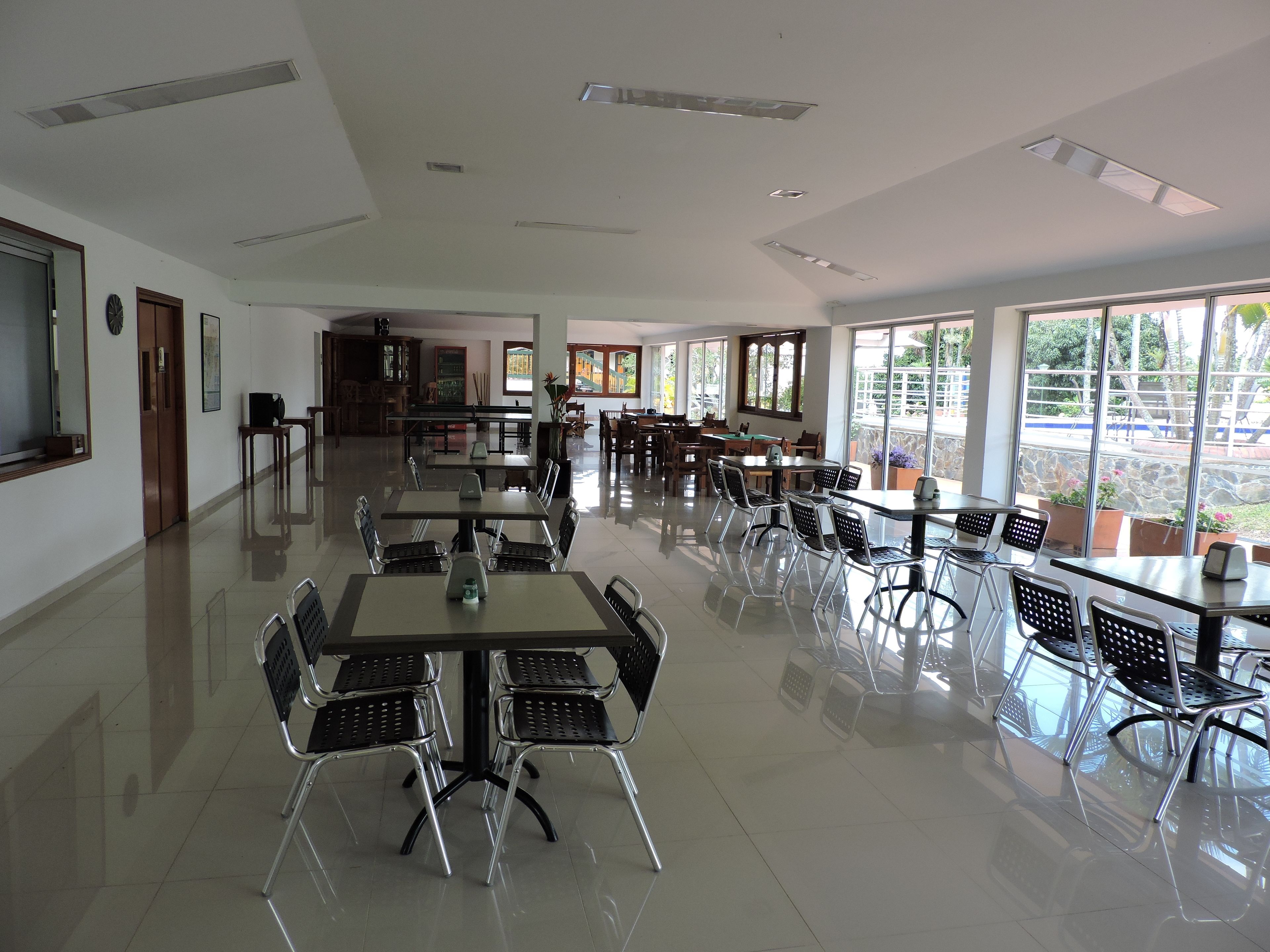 A spacious dining area with multiple tables and chairs, large windows offering views of the outdoors, and a clean, modern interior design.