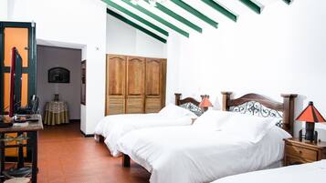 Une chambre d’hôtel avec deux lits, une armoire en bois, une table avec un ventilateur et une lampe.