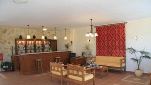 A bar area with stools, a sofa, and a dining table in a room with tiled flooring and patterned walls. - Panos Beach Hotel (Platanias)
