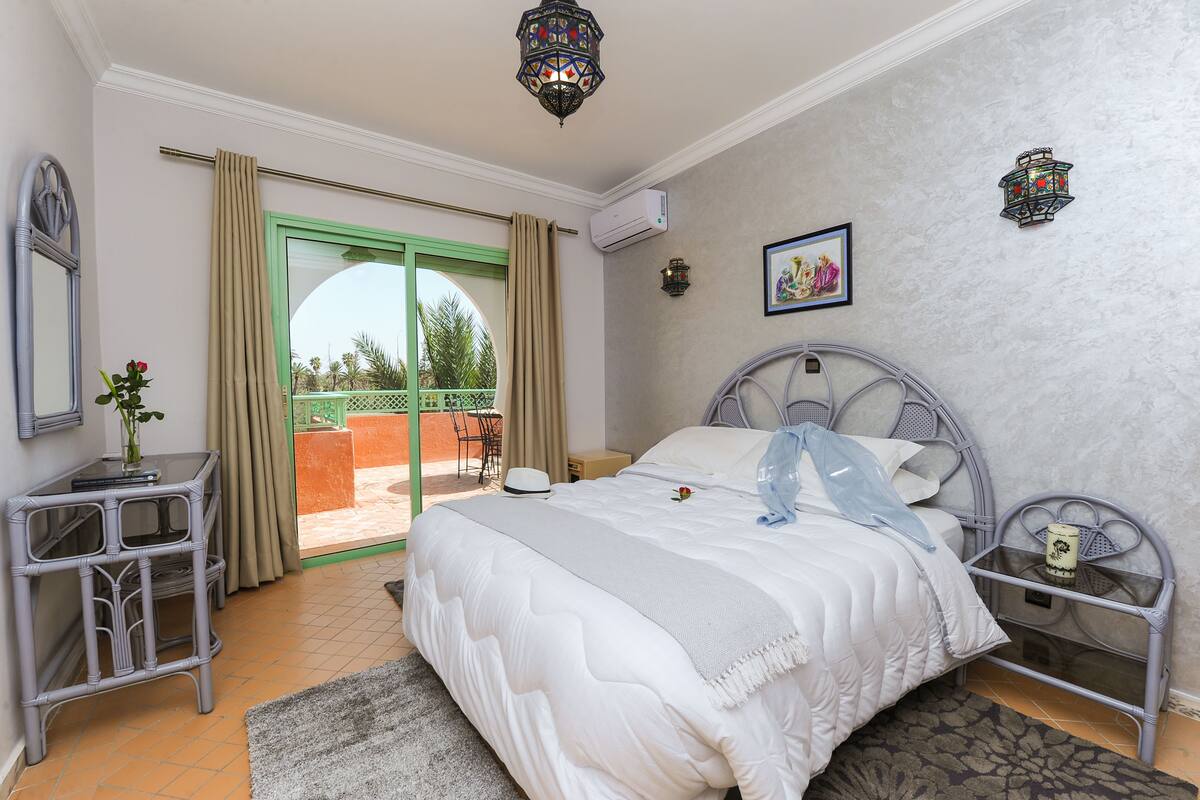 A bedroom with a bed, a nightstand, a dresser, a balcony door, and a view of the outdoors.